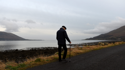 An elderly man walks along the coast in Omeath, Ireland