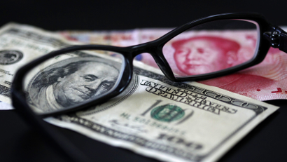 A U.S. dollar note (L) and a Chinese yuan banknote are seen through a pair of spectacles in this picture illustration taken in Taipei October 13, 2010. China's foreign exchange reserves soared in the third quarter and its trade surplus remained hefty, showing that the country is under both economic and political pressure to let the yuan rise more quickly.