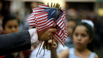 A man hands out U.S. flags at a naturalization ceremony for 3,703 new U.S. citizens from 130 countries, in Los Angeles, California, December 17, 2013.