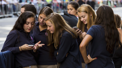 A group of girls exchanging and huddled around their phones