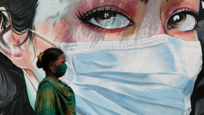 A woman walks past a graffiti of a girl wearing a protective mask amidst the spread of the coronavirus disease (COVID-19) in Mumbai