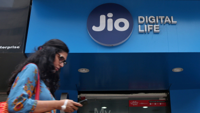 A woman checks her mobile phone as she walks past a mobile store of Reliance Industries' Jio telecoms unit in Mumbai