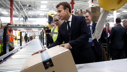 French President Emmanuel Macron (C), flanked by an employee (L) and Amazon French Operations Director Ronan Bole (R), moves a package during a visit at the Amazon factory in Boves, near Amiens, France, October 3, 2017.
