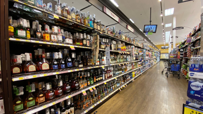 The aisle of a liquor store is filled with bottles of gin, tequila, and whiskey.