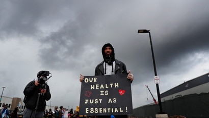 Christian Smalls holds a sign reading "Our health is just as essential."