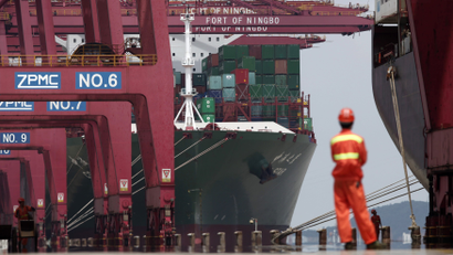 A dockworker in coveralls watches as a container ship is unloaded in the port of Ningbo