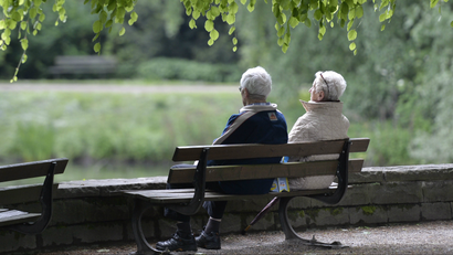 An elderly couple sits on a bench in a park