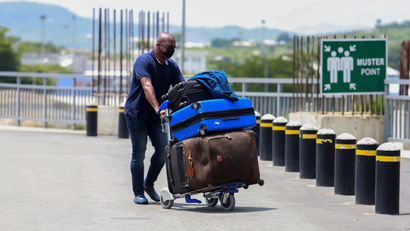 A man pushing three travel bags stacked on a cart through a road in an airport environment