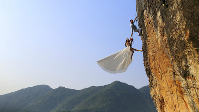 An amateur climber takes wedding pictures with his bride on a cliff