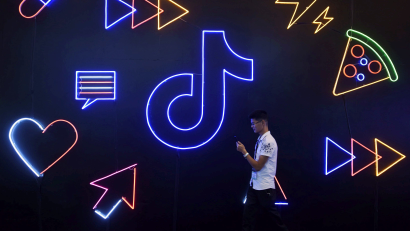 A man holding a phone walks past a sign of Chinese company ByteDance's app TikTok