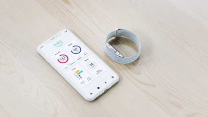 A silver Amazon Halo wristband sits next to a smartphone displaying the sleek Halo app