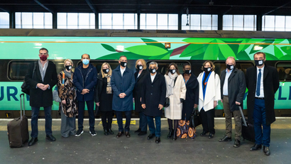 Twelve mayors from cities around the world stand on a train platform in front of a train painted green with leaves