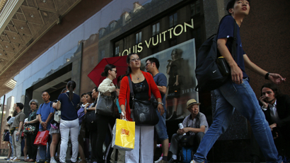 Chinese tourists wait for their bus in front of a fashion store in Paris, Wednesday, Aug. 12, 2015. China's currency fell further Wednesday following a surprise change in its exchange rate mechanism that rattled global markets and threatens to fan trade tensions with the United States and Europe. The central bank said the yuan's 1.9 percent devaluation Tuesday against the U.S. dollar, which was its biggest one-day fall in a decade, was due to changes aimed at making the tightly controlled currency more market-oriented. (AP Photo/Francois Mori)