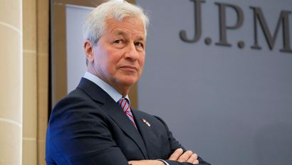 Jamie Dimon crosses his arms in front of the JPMorgan Chase logo.