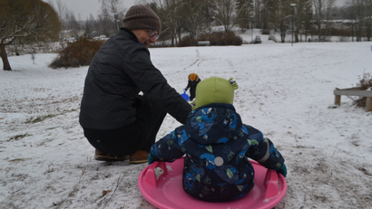 A dad and his son go sledding in the snow.