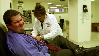 Bob Derboghossian (L) of Chicago, grimaces as phlebotomist Maria Morales (R) inserts a needle to draw blood at Lifesource Blood Center in Chicago, September 12, 2001, as a news program plays on the television in the background, one day after the attack by terrorists on New York City and Washington, D.C. The wait to donate blood was from 2 to 4 hours.