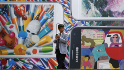 A man uses his mobile phone in front of a giant advertisement promoting Samsung Electronics' new Galaxy S5 smartphone, at an art hall in central Seoul April 15, 2014. Samsung Electronics Co Ltd's new Galaxy S5 smartphone should outsell its predecessor and defy predictions that the South Korean titan's latest model will struggle in a tough market for high-end handsets, Yoon Han-kil, senior vice president of Samsung's product strategy team, told Reuters in an interview. Picture taken on April 15, 2014. To match Interview SAMSUNG-ELEC-SALES/ REUTERS/Kim Hong-Ji