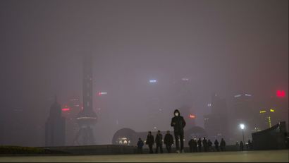 A man wearing an air mask walks through downtown Shanghai, China. The sky is filled with smog.