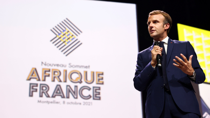 A picture of Emmanuel Macron holding a microphone on stage with a backdrop of the Africa-France summit 2021 behind him