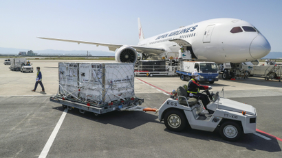 An airport worker carts away boxes of cargo from a passenger plane on a runway.