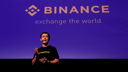 A man in a black T-shirt gestures in front of a purple background written "BINANCE"