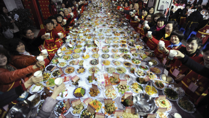 A massive table with food and 20 or so guests down each side raising their glasses.