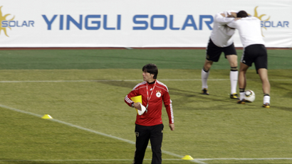 In this file photo taken Tuesday, June 22, 2010, Germany head coach Joachim Loew, front, walks over the pitch as German players stretch during a German team training session near a advertisement panel for Yingli Solar at the Super stadium in Atteridgeville near Pretoria, South Africa. China did not qualify for the World Cup, but the country is still making an appearance in South Africa. An ambitious Chinese solar company, the country's first World Cup sponsor, has placed advertising in all the stadiums in a bid to give its brand a worldwide boost. Yingli Green Energy Co.'s sponsorship deal allows it to show its logo of Yingli Solar, in Chinese and English, on electronic perimeter-boards at all 64 games of the World Cup. (AP Photo/Gero Breloer