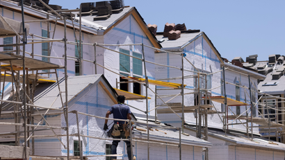 A construction worker stands on scaffolding in front of a house under construction.