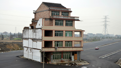 A car stops beside a house in the middle of a newly built road in Wenling, Zhejiang province, November 22, 2012. An elderly couple refused to sign an agreement to allow their house to be demolished. They say that compensation offered is not enough to cover rebuilding costs, according to local media. Their house is the only building left standing on a road which is paved through their village.