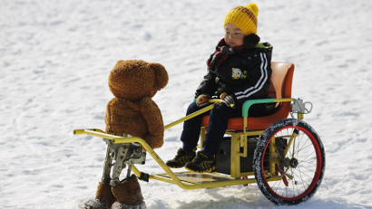 A boy rides on a snow wagon towed by a robot dressed as a Teddy bear, which only moves forward by moving its legs, during the Ice and snow carnival at Taoranting park in Beijing February 9, 2015.