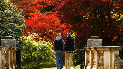 Two men walk hand in hand past changing autumn leaves in Sheffield Park Gardens near Haywards Heath in southern England