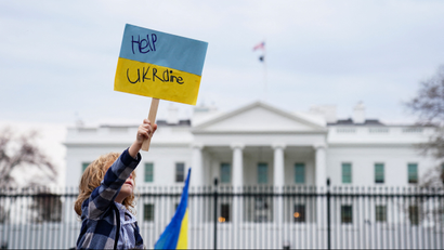 A child holds a homemade sign during a protest against Russia's invasion of Ukraine outside the White House in Washington DC that says "Help Ukraine." The sign is blue and yellow, the Ukrainian flag's colors.