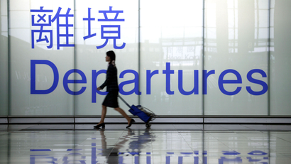 Business traveler wheels luggage past "departures" sign in airport