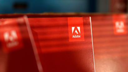 Three red boxes of Adobe software with their logos facing forward are lit by the light from a window.