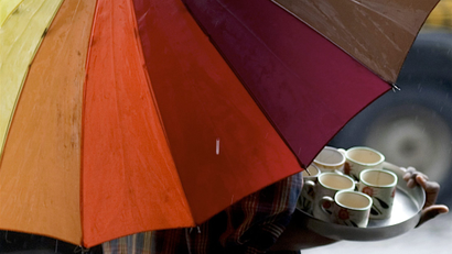 Tea vendor holds umbrella at roadside in Mumbai