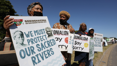 A couple of indigenous women hold signs that protest Amazon's headquarters in South Africa