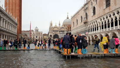 People walk on a catwalk in a flooded Saint Mark Square during a period of seasonal high water in Venice