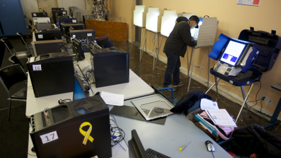 A man fills out a ballot at a booth inside an internet cafe, behind a row of computers.