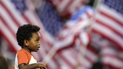 A child stands in front of multiple US flags