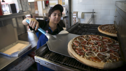 A worker takes a pizza out of the oven at a Domino's Pizza