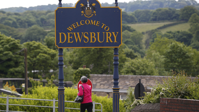 A woman walks past a sign welcoming visitors to Dewsbury in Yorkshire, northern England