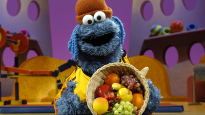 Cookie Monster holding a basket of vegetables and fruit