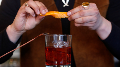 A bartender squeezes a slice of orange above a cocktail