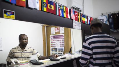 A man in a money-changing shop decorated by many flags, including those of African countries, attends to a customer