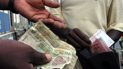 Two people exchanging African currencies, with one person brining a few bills from a wallet