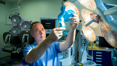 Surgeon Calvin Coffey holds up a 3D plastic model of the mesentery in an operating room.