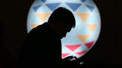 FILE - In this Sunday, Nov. 15, 2015, file photo, a Filipino checks his smartphone in front of the logo of APEC 2015 in Manila, Philippines. (AP Photo/Aaron Favila, File)
