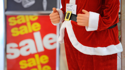 A Santa Claus in front of a Christmas sale sign