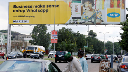 People stand near an advertising billboard for MTN telecommunication company along a street in Abuja