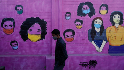 A man wearing a protective face mask walks past a mural on a street, amidst the spread of COVID-19, in Mumbai